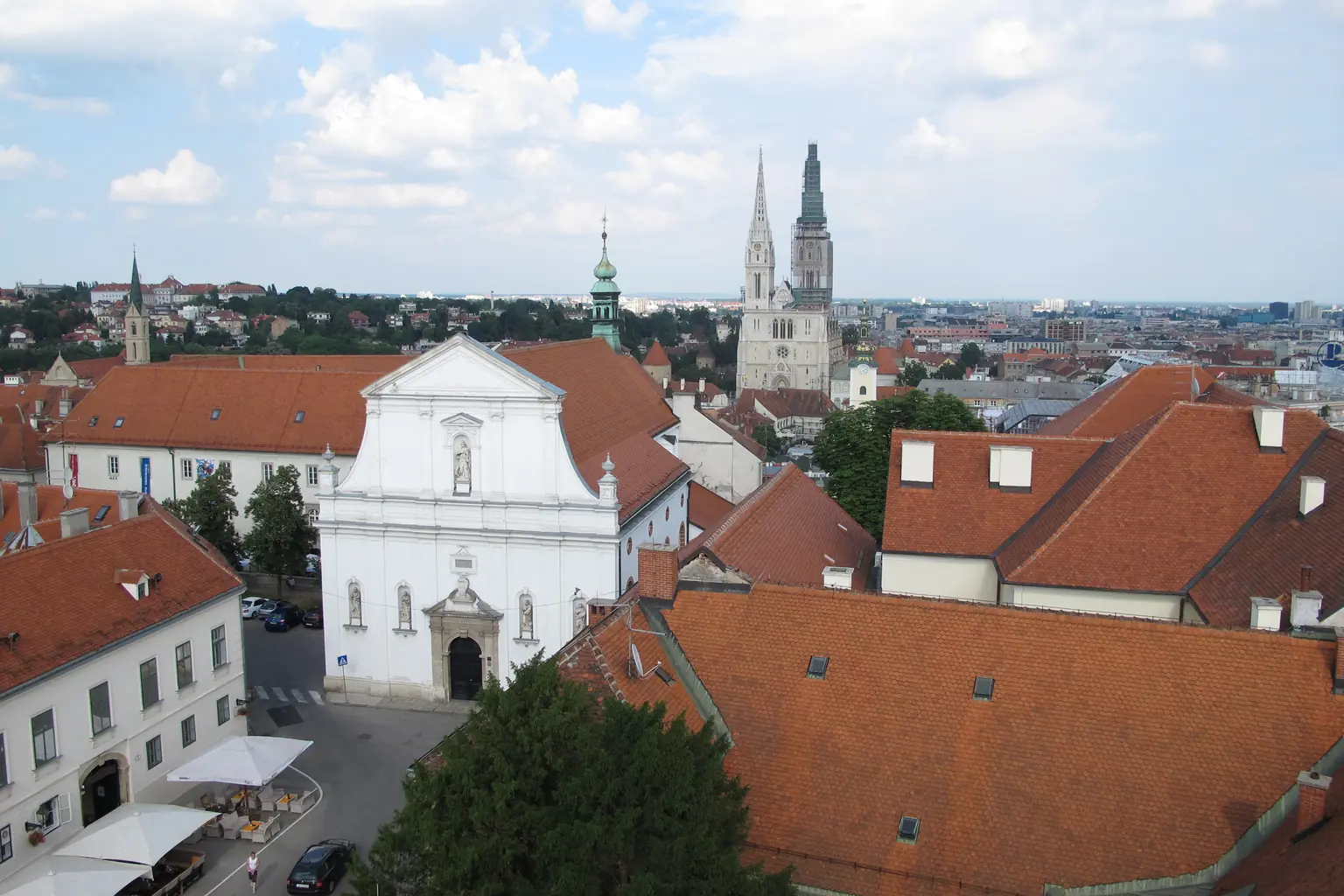 Crveni krovovi zagrebačkoga Gornjeg grada snimljeni odozgo, s bijelom baroknom crkvom i Zagrebačkom katedralom u daljini.